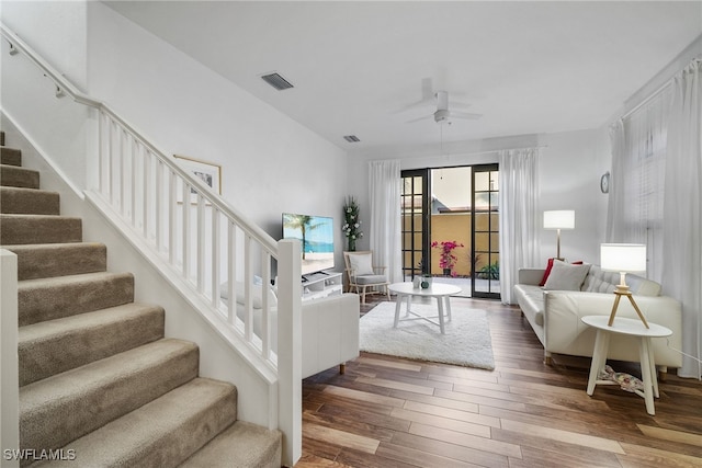 living area with a ceiling fan, stairs, visible vents, and wood finished floors