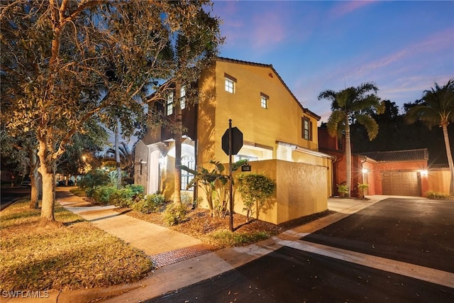 property exterior at dusk featuring a garage, an outbuilding, and stucco siding