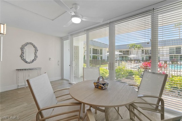 dining room featuring light wood-style floors, a ceiling fan, baseboards, and a wall of windows