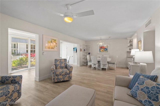 living room featuring a ceiling fan, light wood-style flooring, visible vents, and baseboards