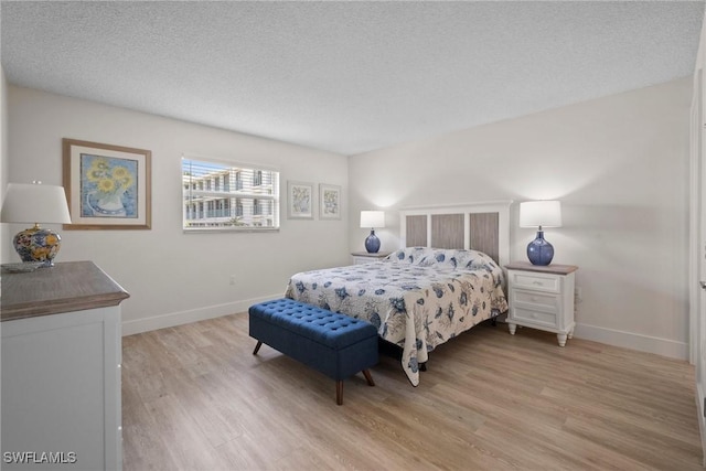 bedroom with light wood-type flooring, baseboards, and a textured ceiling