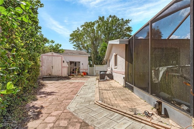 view of patio featuring an outbuilding, glass enclosure, fence, and a storage unit