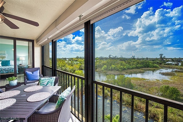 balcony featuring a water view, a sunroom, and a ceiling fan