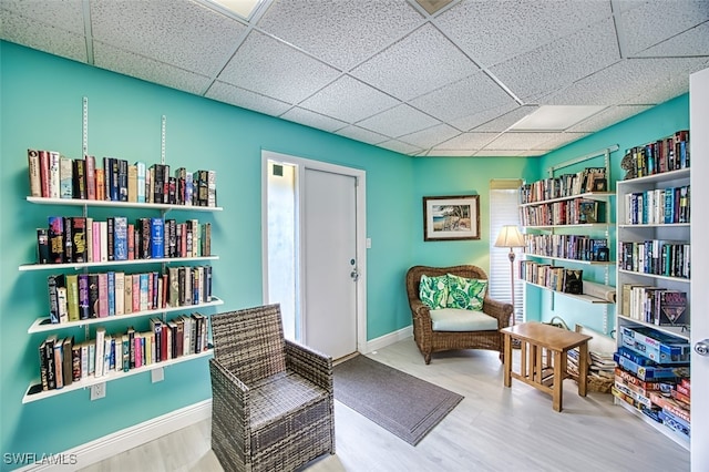 sitting room with a drop ceiling, wood finished floors, and baseboards