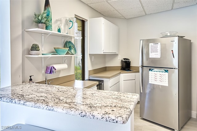 kitchen featuring open shelves, light countertops, freestanding refrigerator, a drop ceiling, and a peninsula