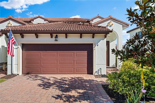 mediterranean / spanish-style home with a garage, a tile roof, decorative driveway, and stucco siding