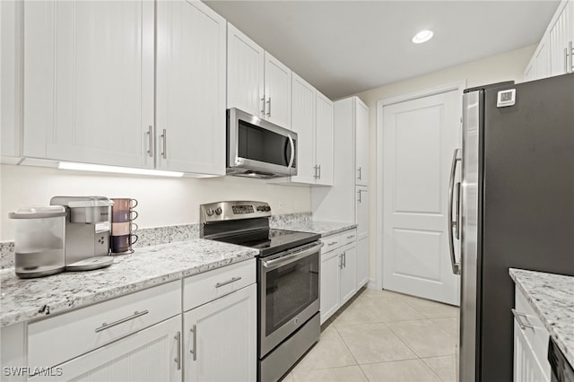 kitchen with light tile patterned floors, appliances with stainless steel finishes, light stone countertops, and white cabinets