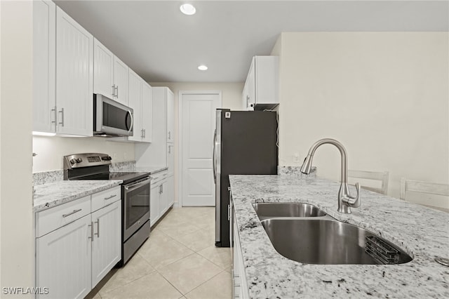 kitchen with light stone counters, light tile patterned floors, appliances with stainless steel finishes, white cabinetry, and a sink