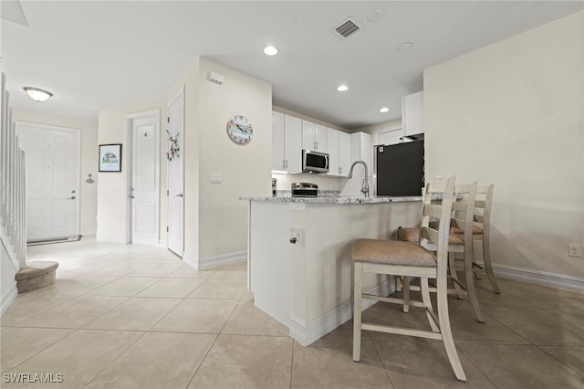 kitchen featuring light tile patterned flooring, refrigerator, a peninsula, visible vents, and stainless steel microwave