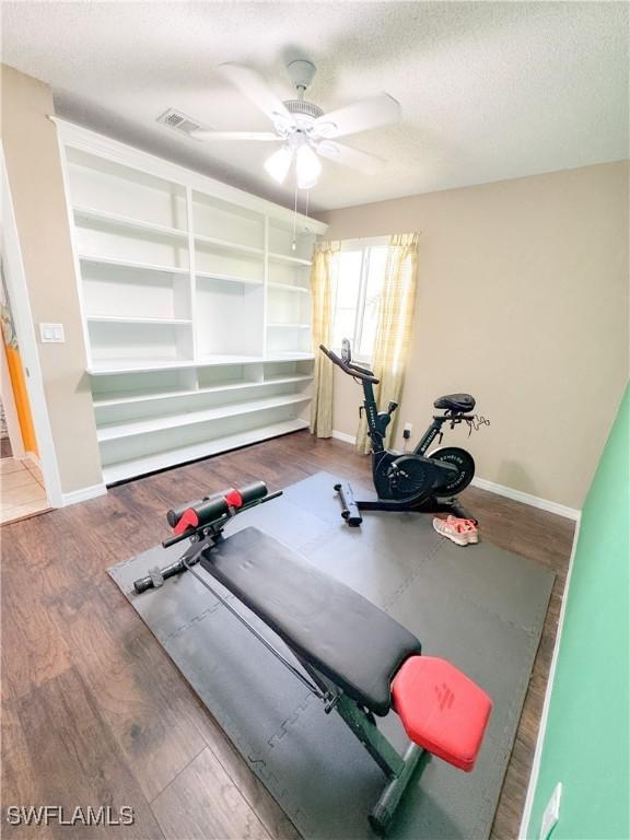 workout area featuring a ceiling fan, a textured ceiling, baseboards, and wood finished floors