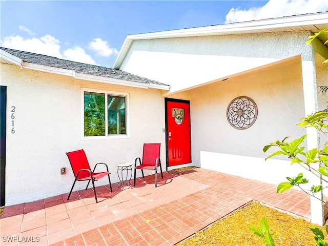 doorway to property with roof with shingles, a patio, and stucco siding