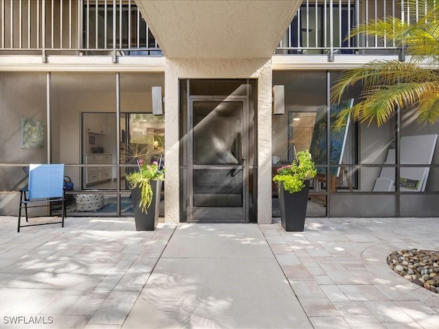 property entrance featuring a balcony, a patio area, and stucco siding