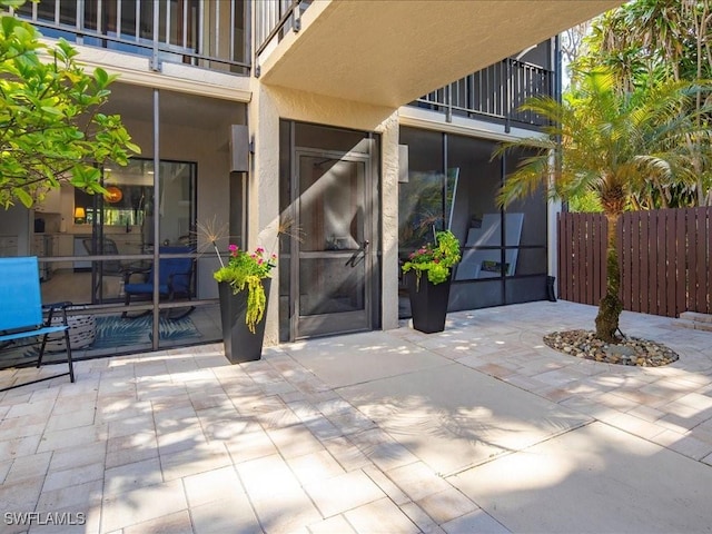 entrance to property with a patio, fence, a balcony, and stucco siding