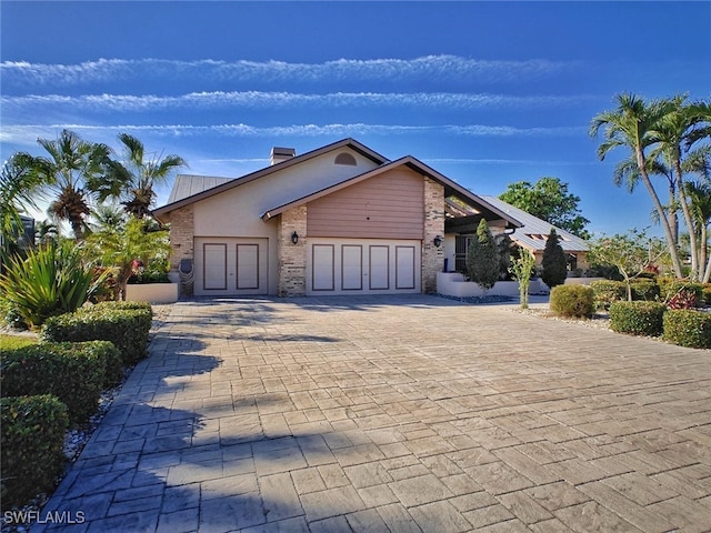 view of front facade with a garage, a chimney, decorative driveway, and brick siding