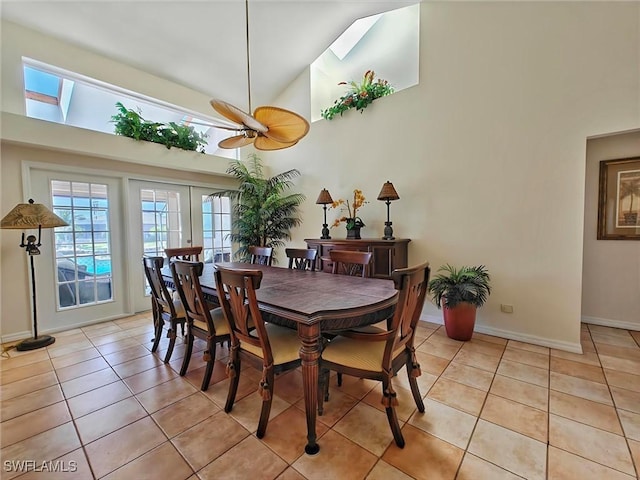 dining area featuring a skylight, french doors, light tile patterned flooring, high vaulted ceiling, and baseboards