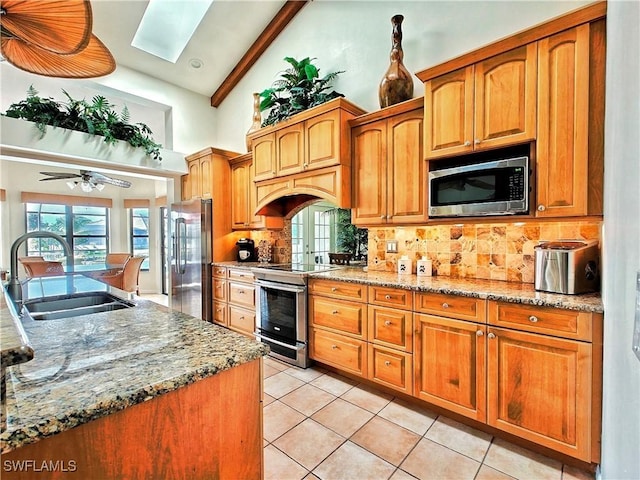 kitchen with a skylight, a sink, appliances with stainless steel finishes, light stone countertops, and tasteful backsplash