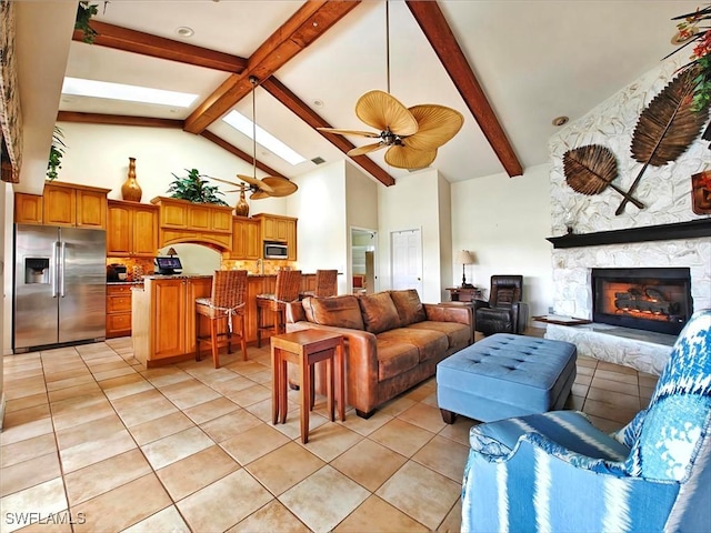 living area with light tile patterned floors, a skylight, ceiling fan, a stone fireplace, and high vaulted ceiling