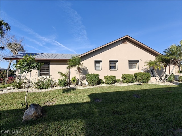 view of side of home with metal roof, central air condition unit, a lawn, and stucco siding