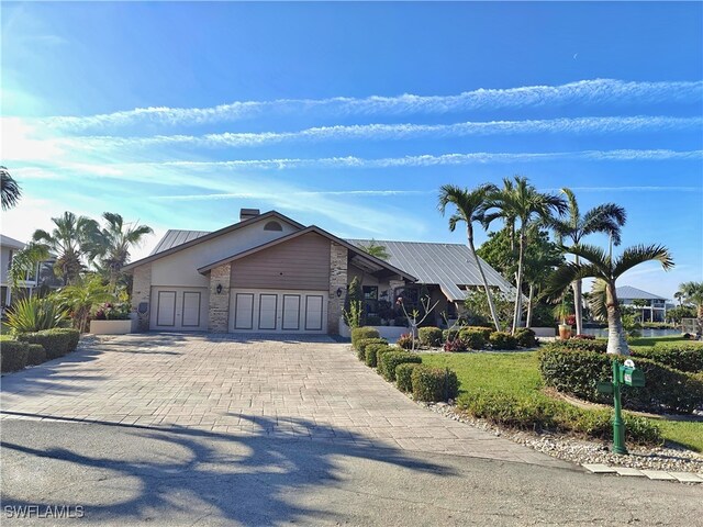 view of front of property featuring a front lawn, decorative driveway, metal roof, and an attached garage