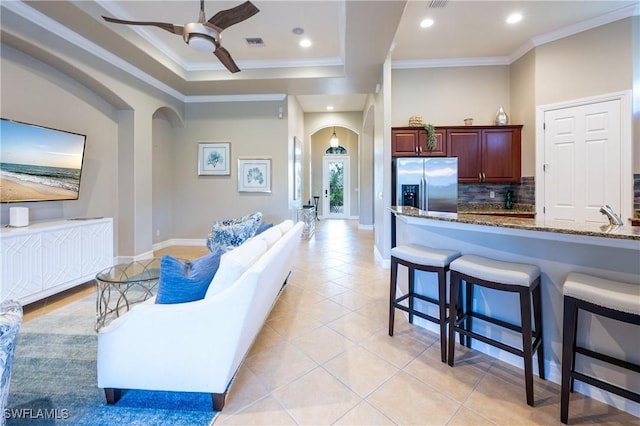 living area featuring arched walkways, ceiling fan, light tile patterned flooring, visible vents, and ornamental molding