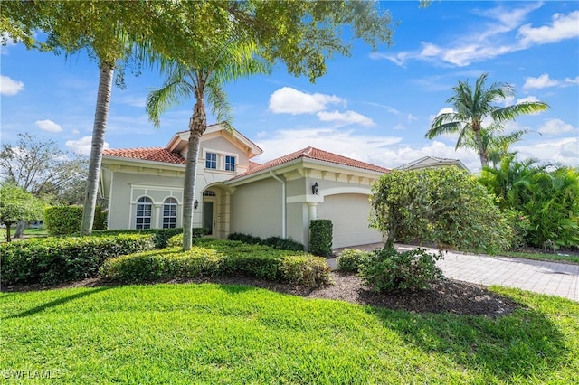 mediterranean / spanish home featuring a tiled roof, a front lawn, an attached garage, and stucco siding