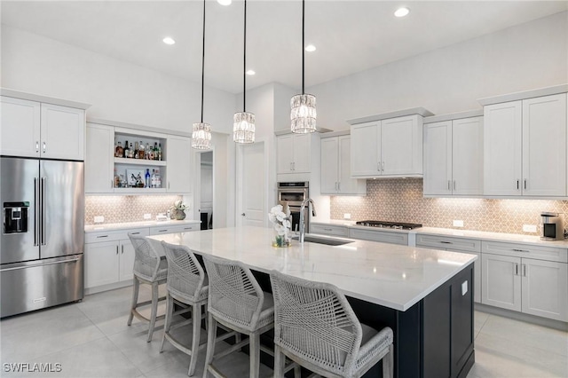 kitchen with light tile patterned flooring, stainless steel appliances, a sink, open shelves, and a center island with sink