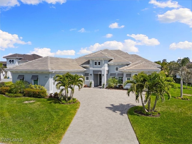 view of front of property with an attached garage, a tile roof, decorative driveway, stucco siding, and a front yard