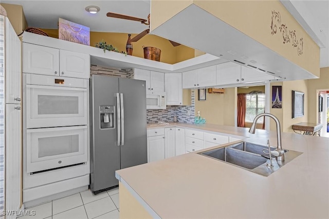 kitchen featuring white appliances, light tile patterned floors, a peninsula, white cabinetry, and a sink