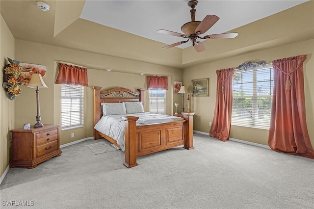 bedroom with a tray ceiling, light colored carpet, baseboards, and multiple windows