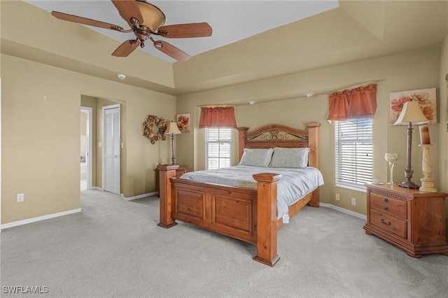 bedroom featuring a raised ceiling, light carpet, ceiling fan, and baseboards