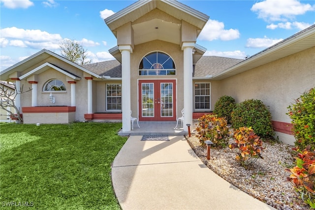 view of exterior entry featuring roof with shingles, french doors, a lawn, and stucco siding