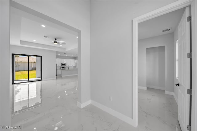 corridor featuring visible vents, baseboards, a tray ceiling, recessed lighting, and marble finish floor