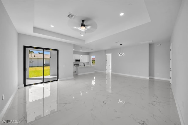 spare room with a raised ceiling, baseboards, visible vents, and ceiling fan