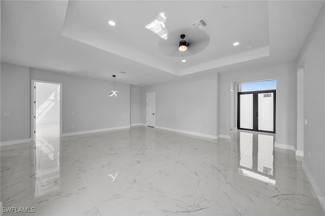 empty room featuring a tray ceiling, baseboards, visible vents, and marble finish floor