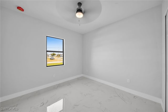 empty room with marble finish floor, a ceiling fan, and baseboards