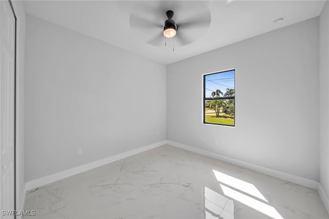 spare room featuring marble finish floor, a ceiling fan, and baseboards