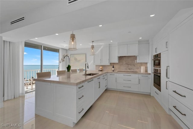 kitchen with tasteful backsplash, expansive windows, white cabinets, a sink, and a peninsula