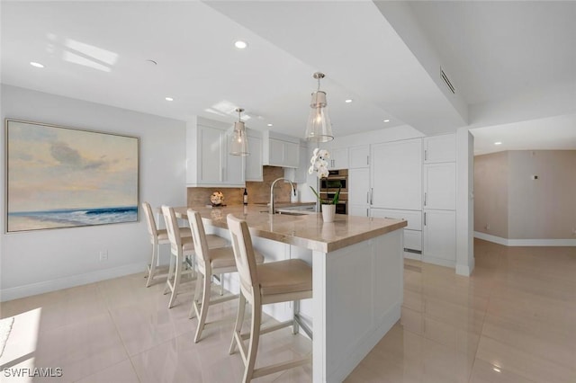 kitchen with light countertops, backsplash, white cabinetry, a sink, and a peninsula