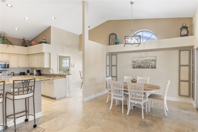 kitchen featuring a chandelier, light stone counters, stainless steel appliances, high vaulted ceiling, and a sink