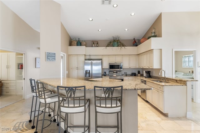 kitchen with a large island, a breakfast bar area, stainless steel appliances, a high ceiling, and a sink