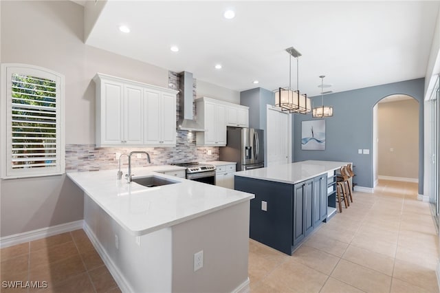 kitchen with arched walkways, a center island, appliances with stainless steel finishes, a sink, and wall chimney range hood