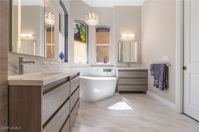 full bath with marble finish floor, two vanities, a freestanding bath, an inviting chandelier, and a sink