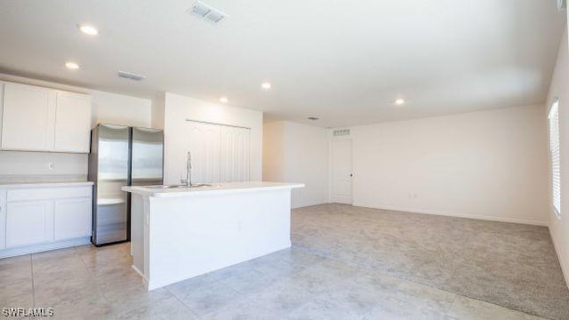 kitchen featuring light countertops, freestanding refrigerator, white cabinetry, and a center island with sink