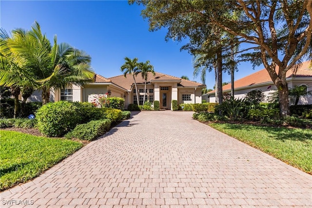 mediterranean / spanish home with a garage, a tile roof, decorative driveway, and stucco siding