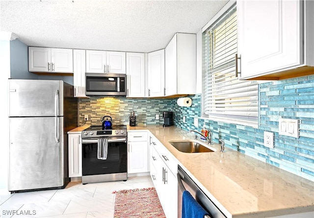 kitchen with a sink, stainless steel appliances, light stone counters, and white cabinets