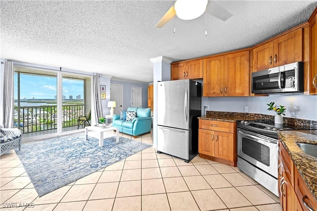 kitchen with stainless steel appliances, dark stone counters, brown cabinets, and light tile patterned floors