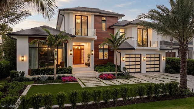 view of front facade featuring decorative driveway, stucco siding, a balcony, a garage, and a tiled roof