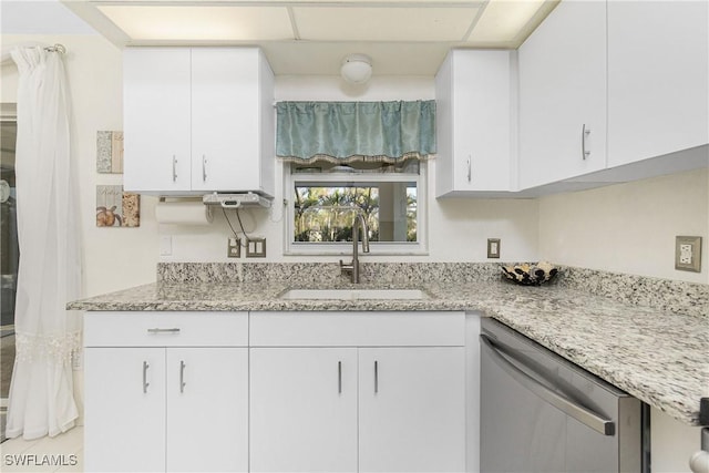 kitchen with stainless steel dishwasher, a sink, white cabinetry, and light stone countertops