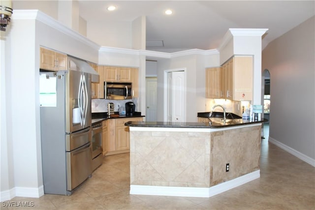 kitchen featuring arched walkways, appliances with stainless steel finishes, backsplash, light brown cabinetry, and a sink