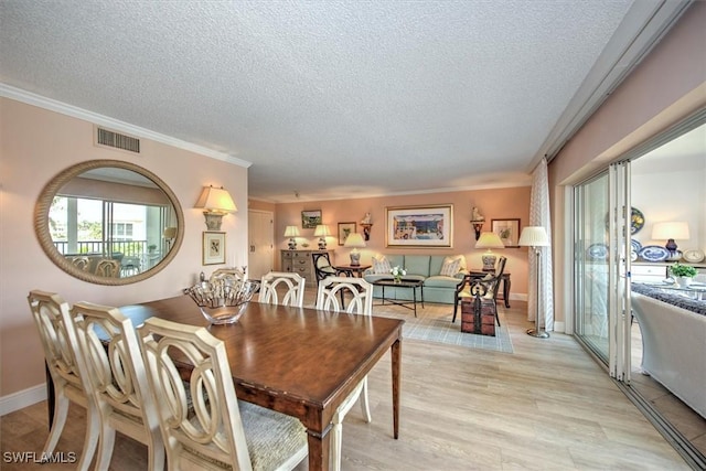 dining space featuring a textured ceiling, light wood-style flooring, ornamental molding, and visible vents